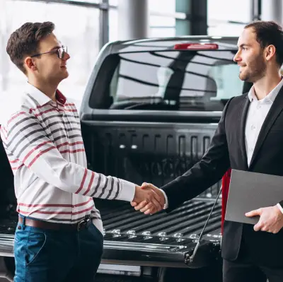img-2 - new Two individuals shake hands in front of a parked pickup truck, symbolizing a business agreement or sale.