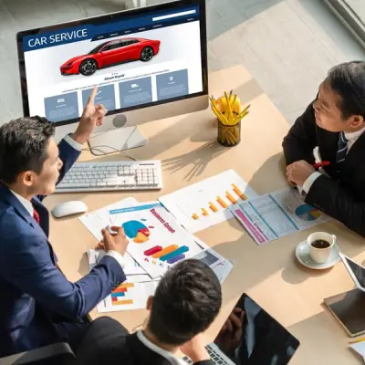 img-4-1 - new A group of business professionals in suits discussing car service data with charts and graphs, a computer displaying a car website.